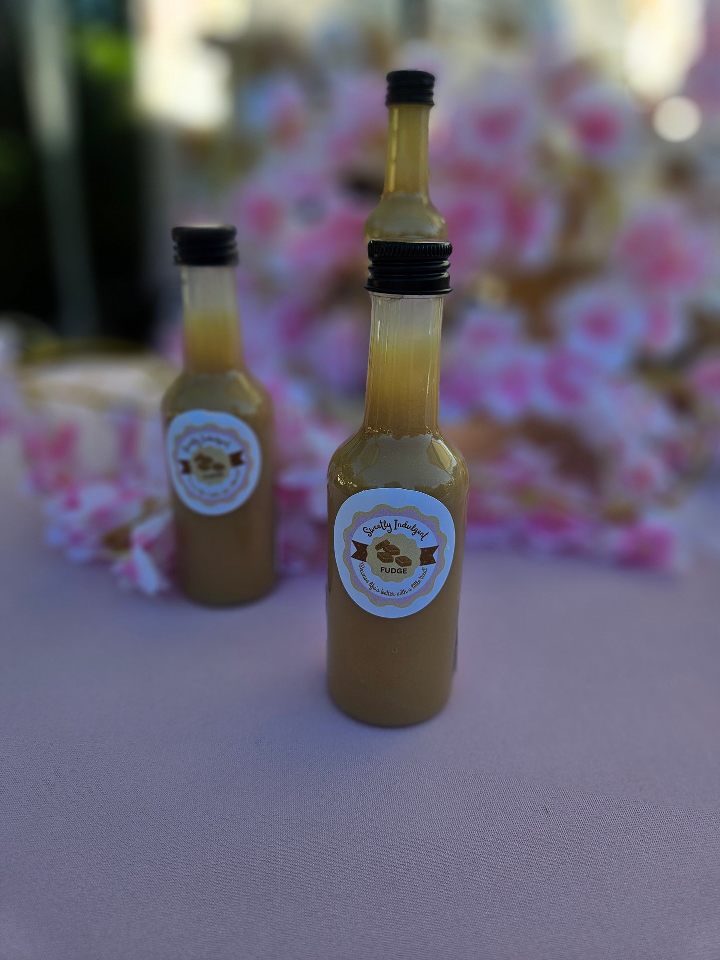 3 fudge sauce bottles on pink table