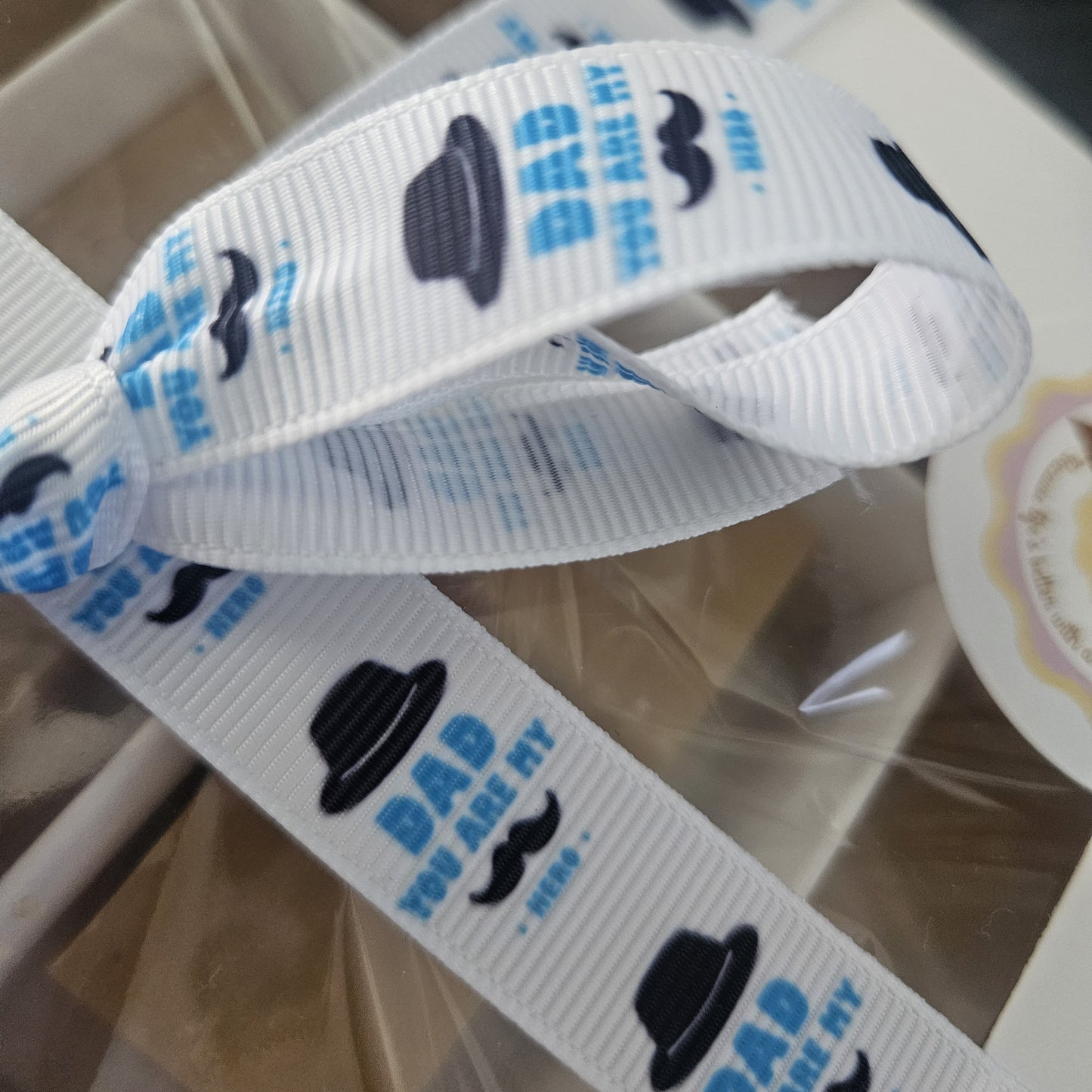 White ribbon with black hats and blue text saying dad you are my hero