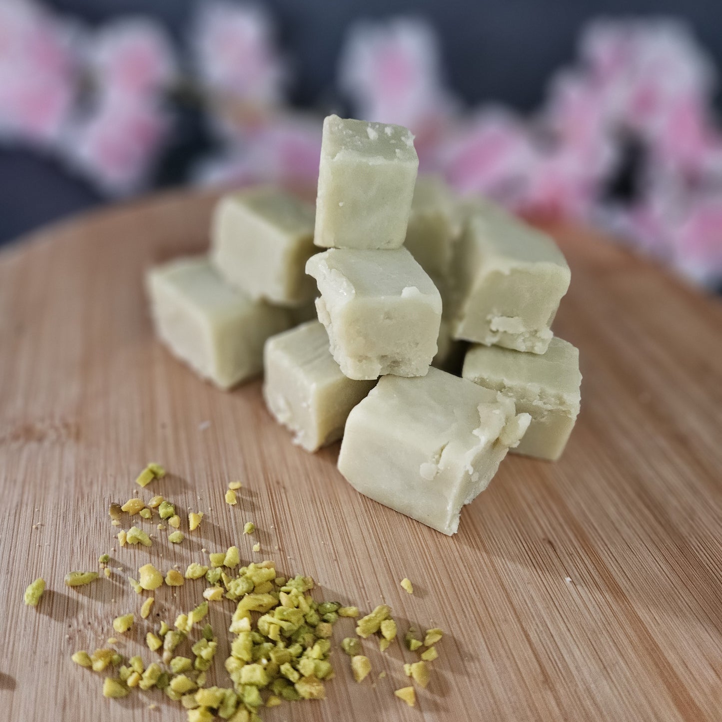 Creamy pistachio fudge cubes on a wooden board with chopped pistachio on wooden board.