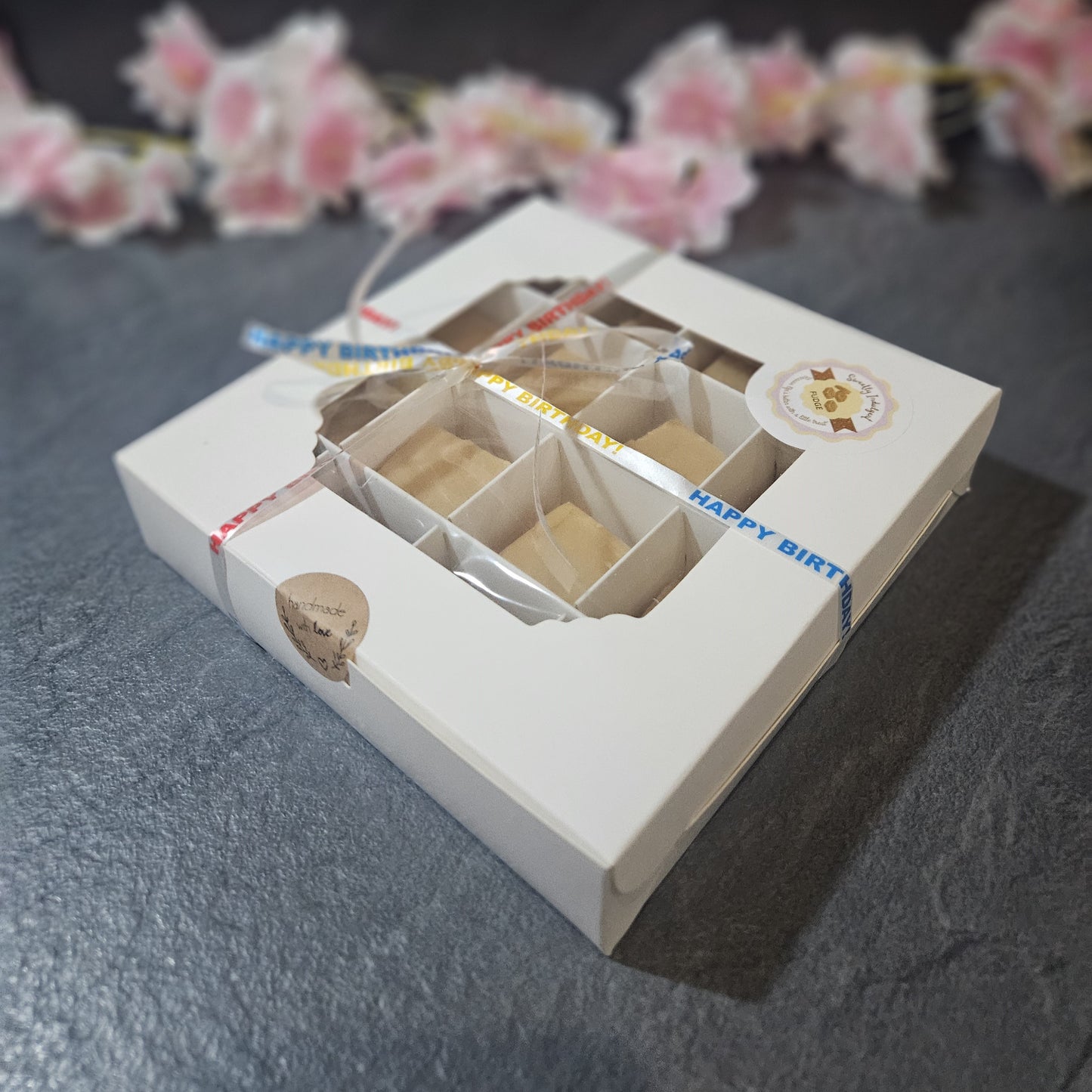 white homemade fudge gift box with compartments on a dark surface with pink flowers in the background