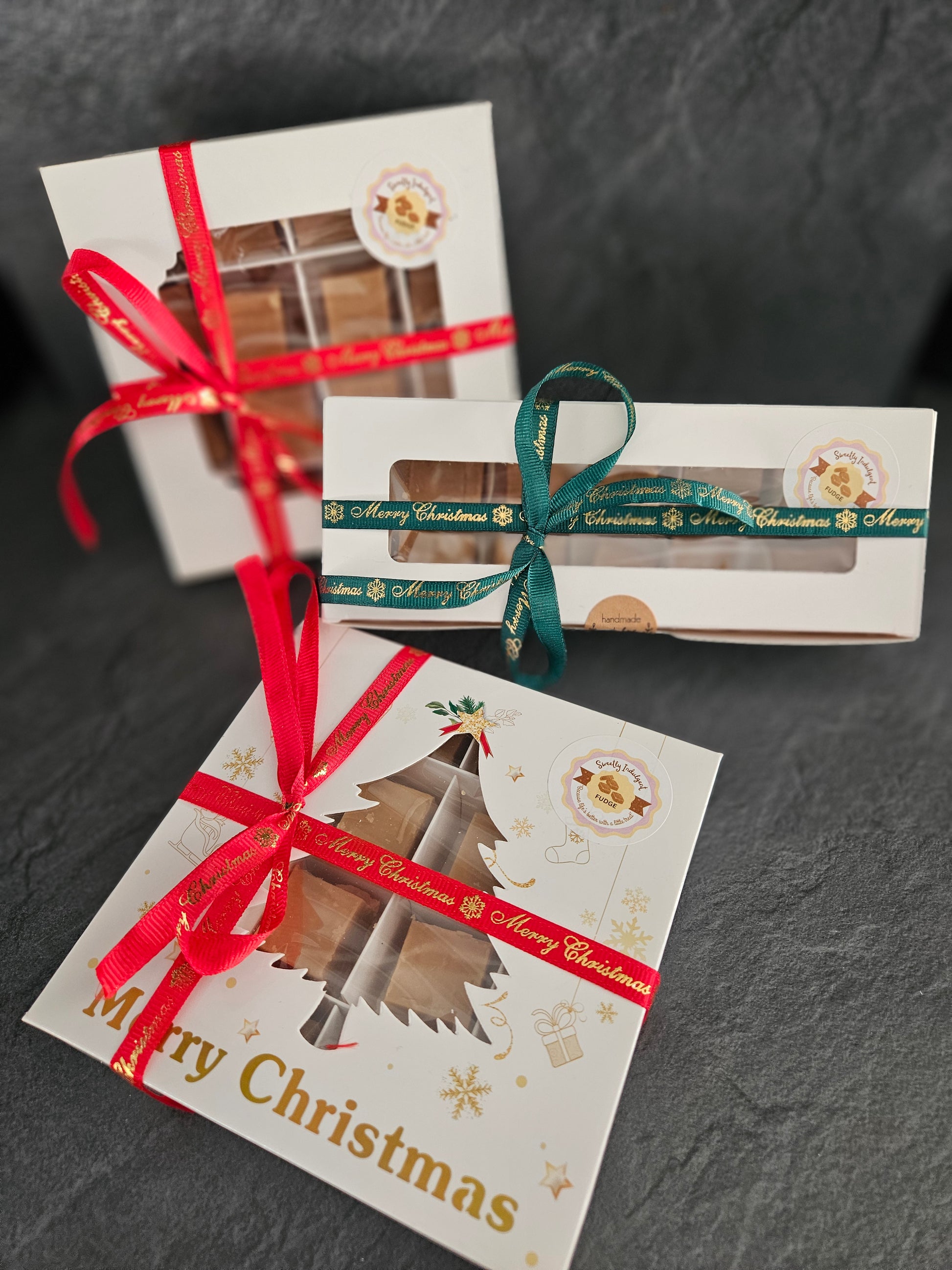 Three gift boxes with festive ribbons and 'Merry Christmas' text on a dark surface