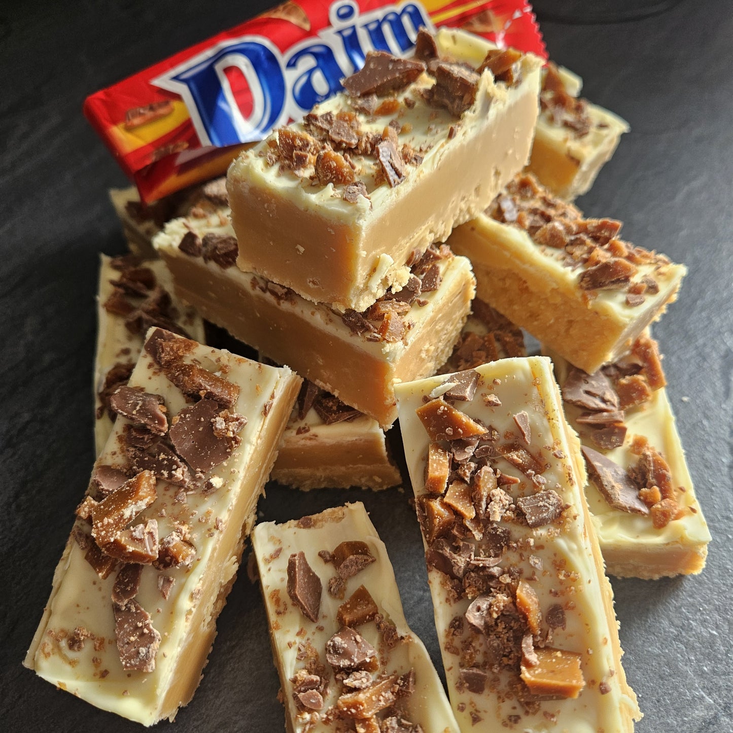 Daim fudge bar with a Daim chocolate bar in the background on a dark surface