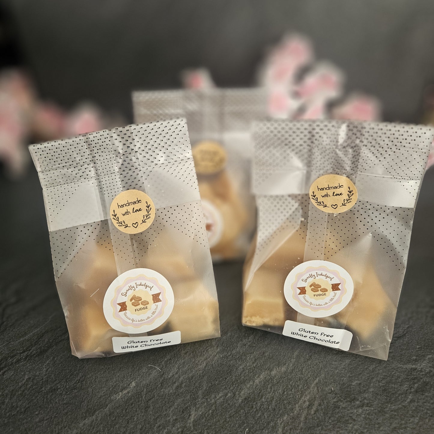 Three clear packaging bags with Sweetly Indulgent logo on a dark surface