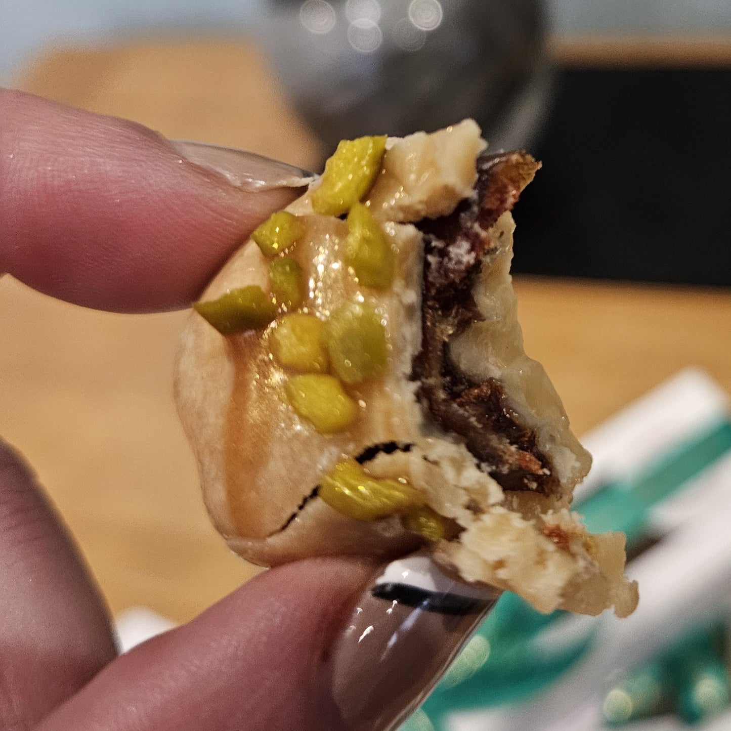 Close-up of a hand holding a piece of fudge dipped Medjool date with pistachios and chocolate drizzle.