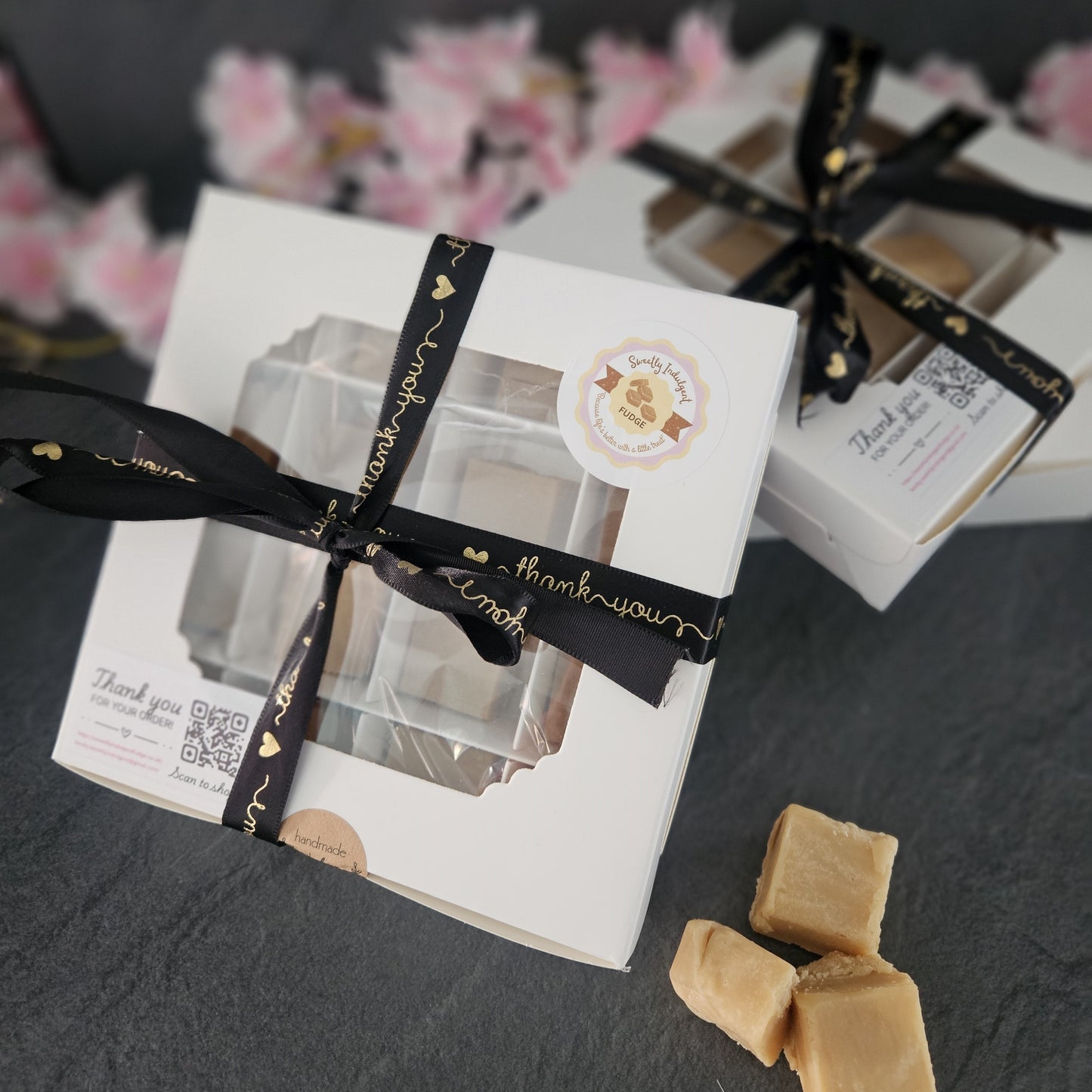 Gift box with black ribbon and fudge on a grey worktop.