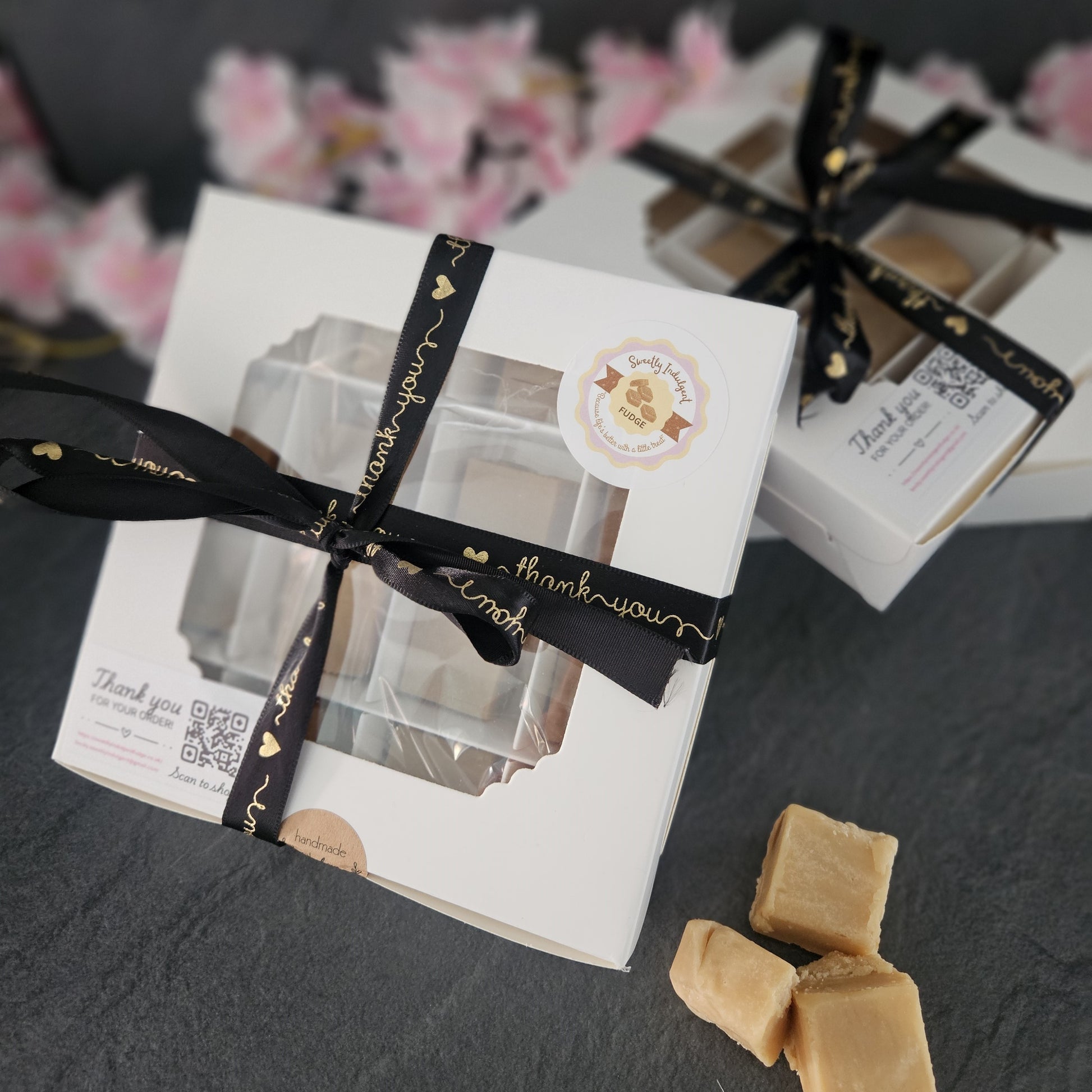Gift box with black ribbon and fudge on a grey worktop.