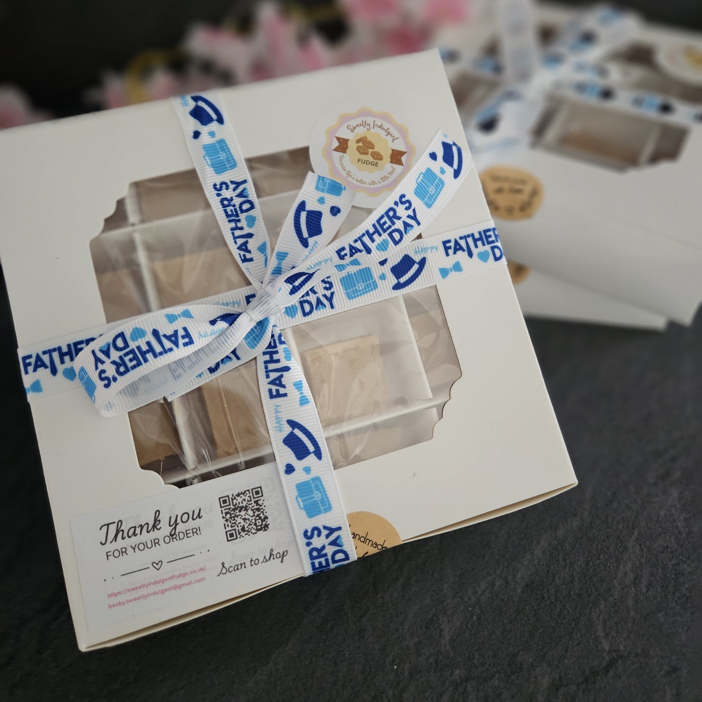 White gift box with a blue Love dad ribbon on a dark surface with other boxes in background.