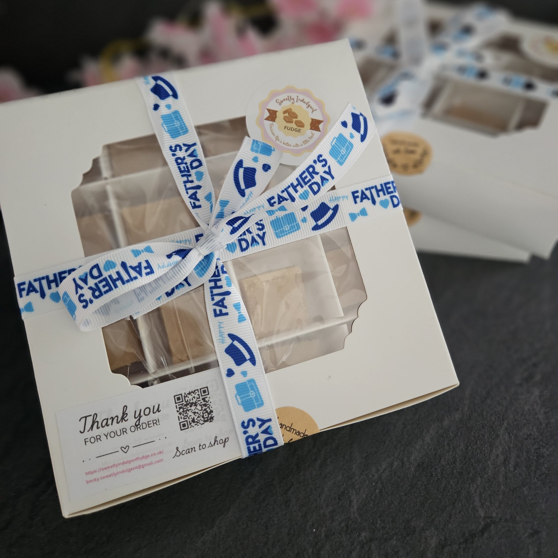 White gift box with a blue Love dad ribbon on a dark surface with other boxes in background.
