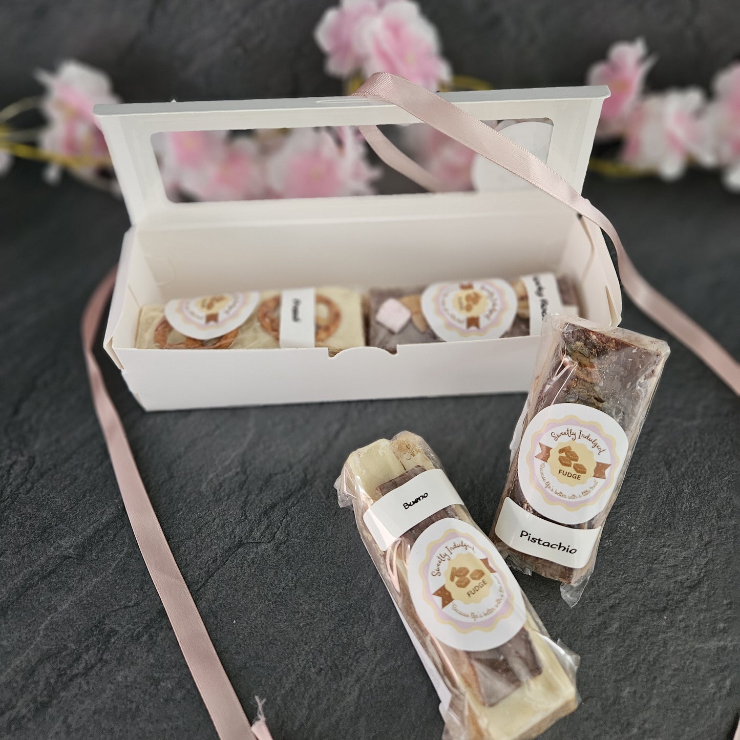 large fudge topping bars with white and milk chocolate with visible branding on a dark surface with pink flowers in the background.
