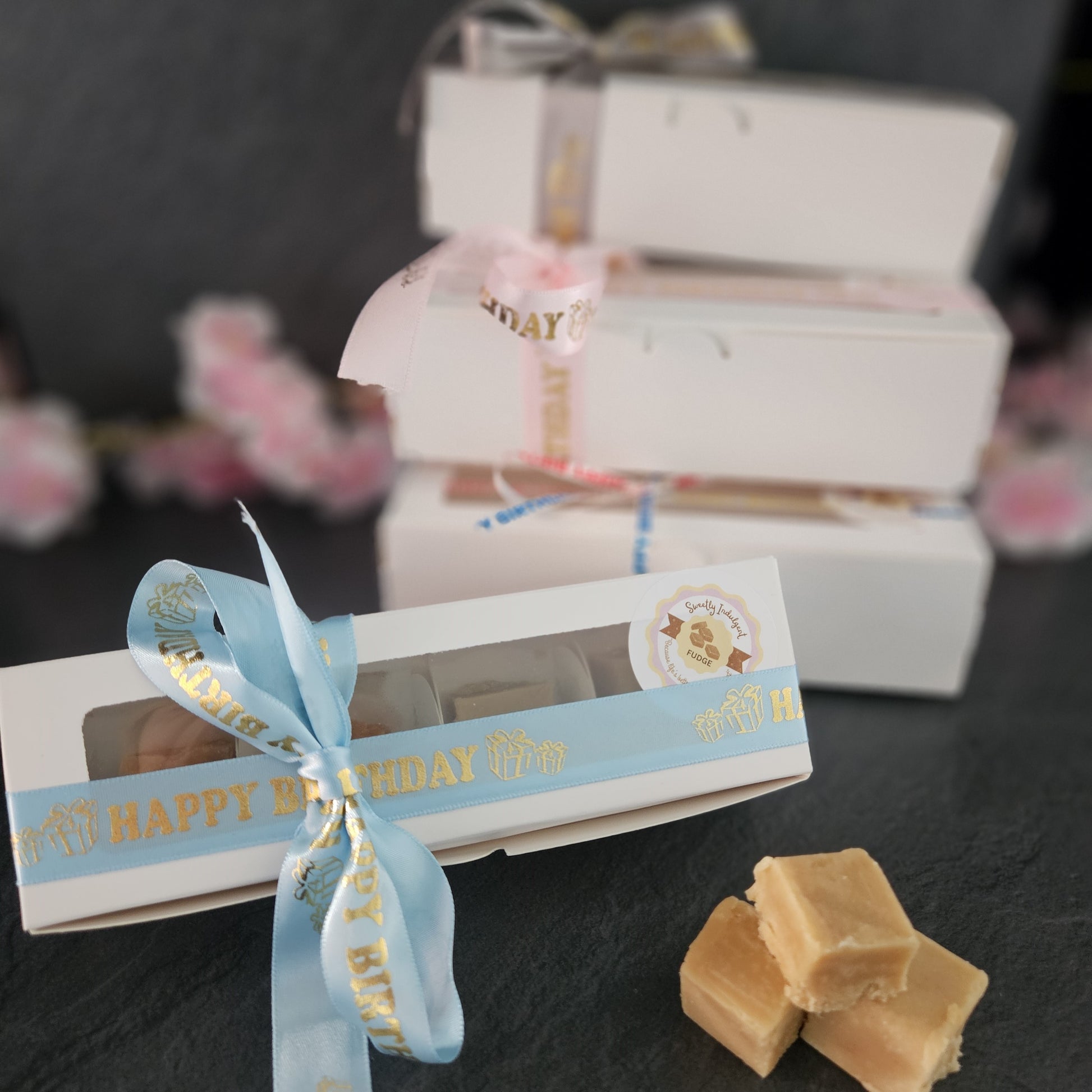 Box of fudge with a 'Happy Birthday' ribbon. Three more stacked boxes in background