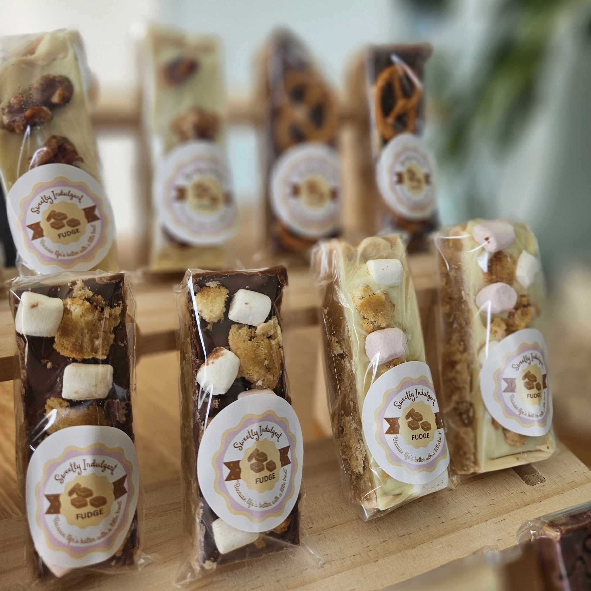Packaged fudge bars with various toppings of pretzel, pistachio and rocky road with visible sweetly indulgent brand labels on a wooden surface