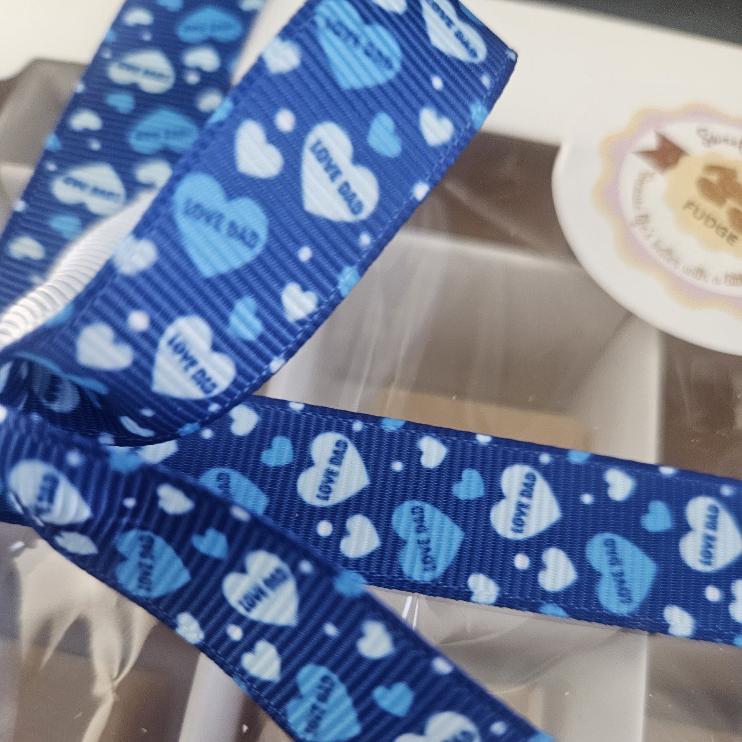 A close up of blue ribbon with love hearts saying love dad on box of fudge