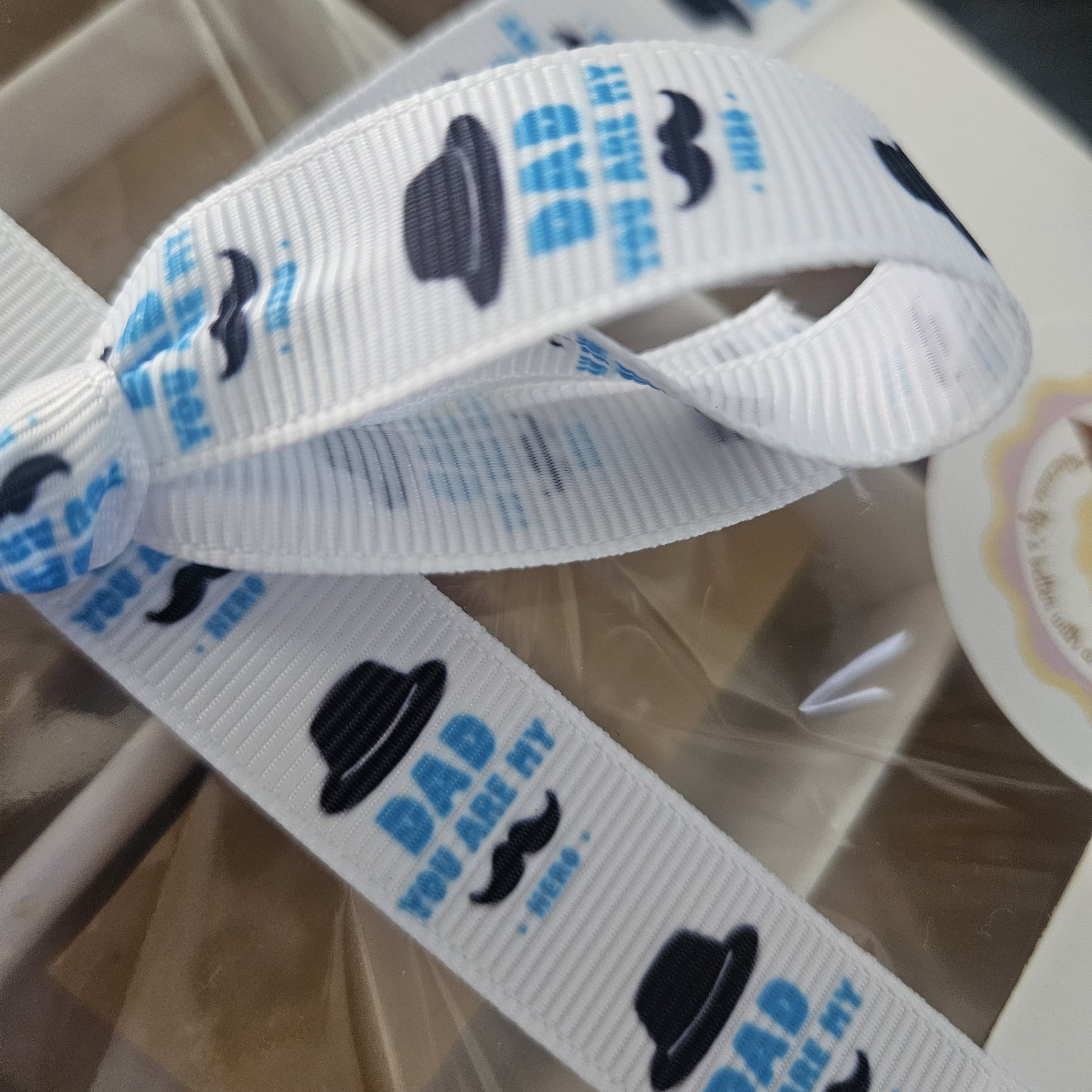 White ribbon with black hats and blue text saying dad you are my hero