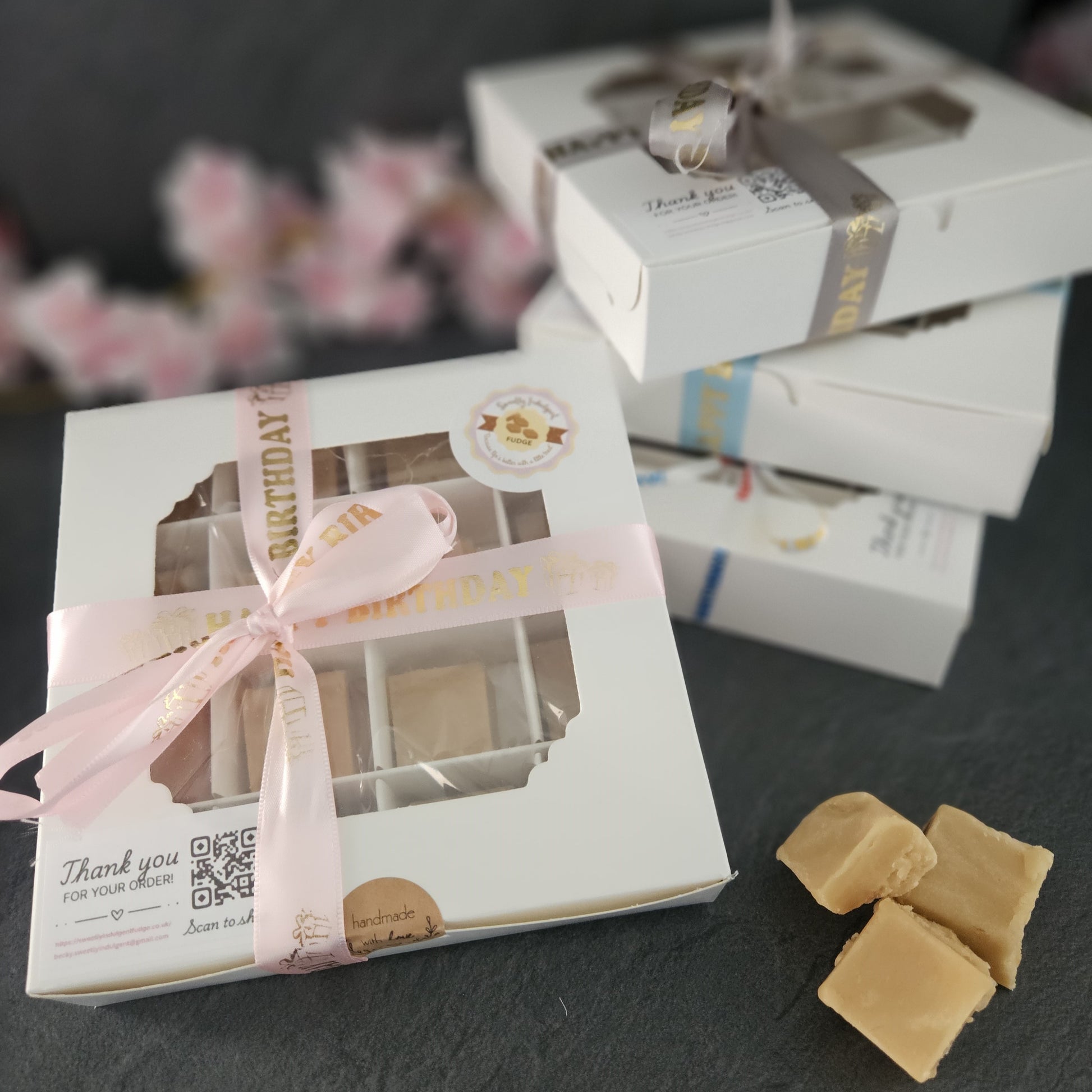 Gift box with a happy birthday pink ribbon and visible fudge contents with pink flowers in background