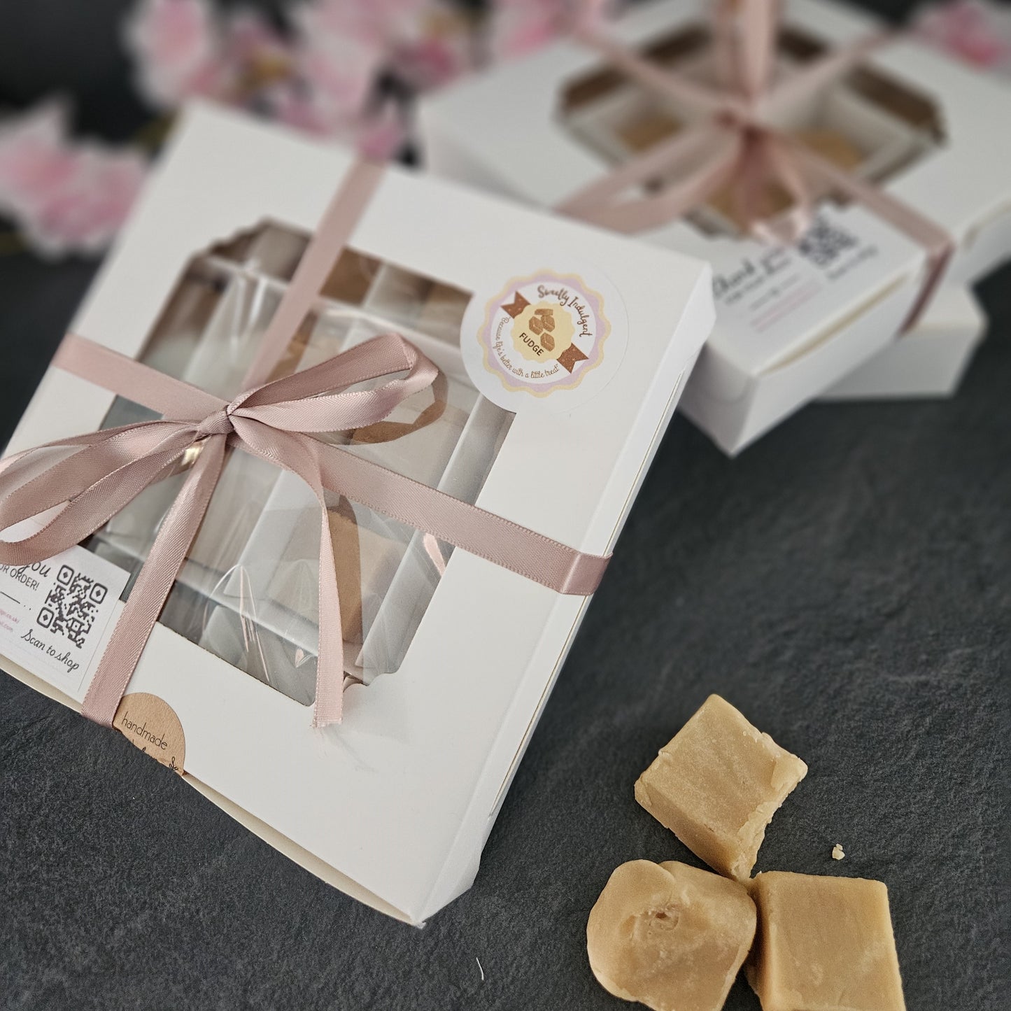 Gift box containing fudge with a pink ribbon and sweetly indulgent logo on a dark surface