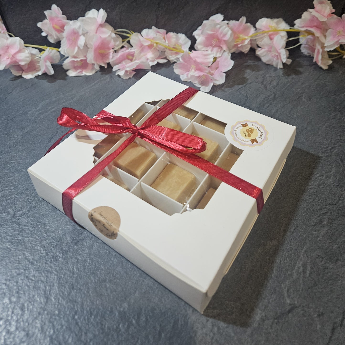 White fudge box with a red ribbon containing Square fudge pieces.