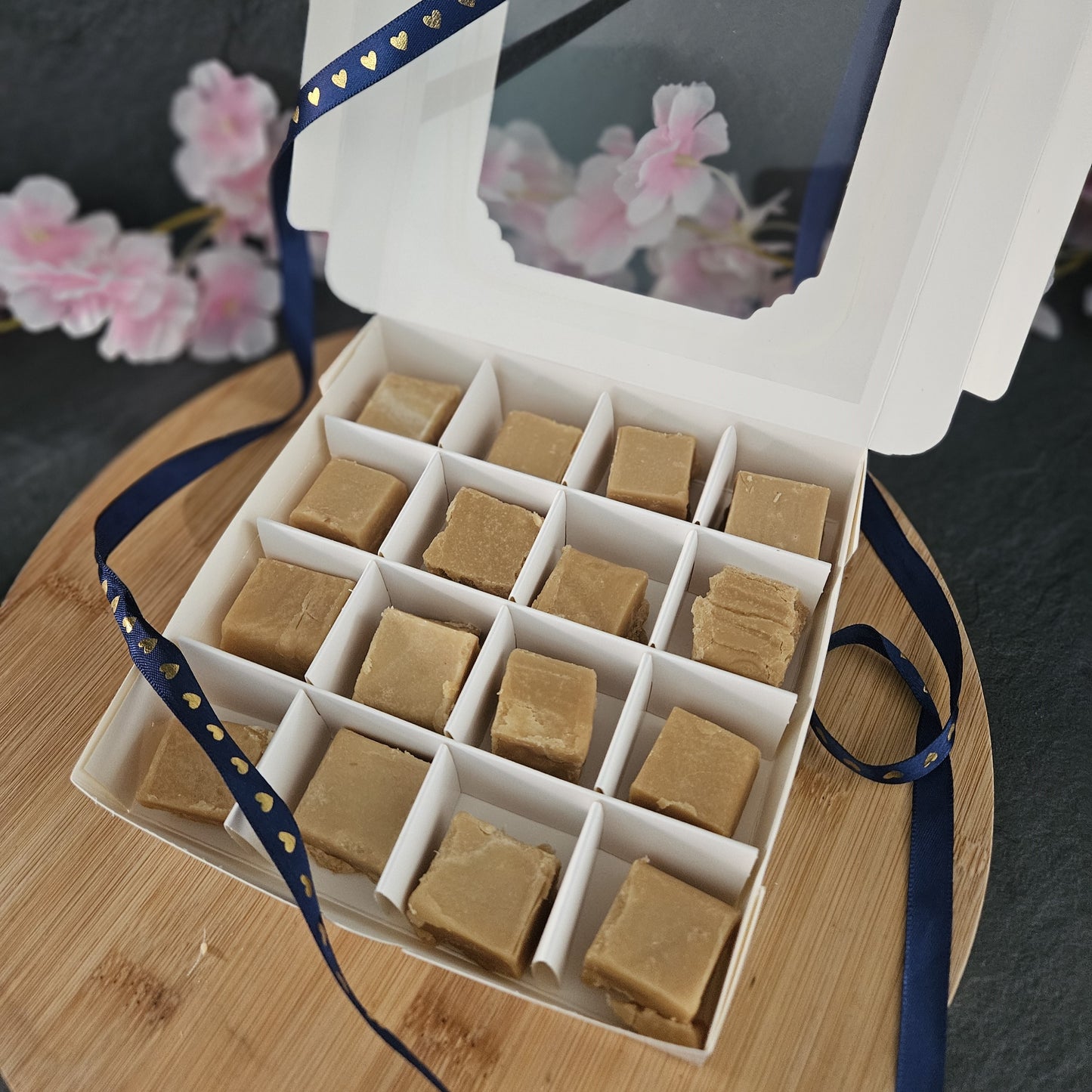 Box of fudge containing 16 pieces with a blue ribbon with gold hearts on a wooden board