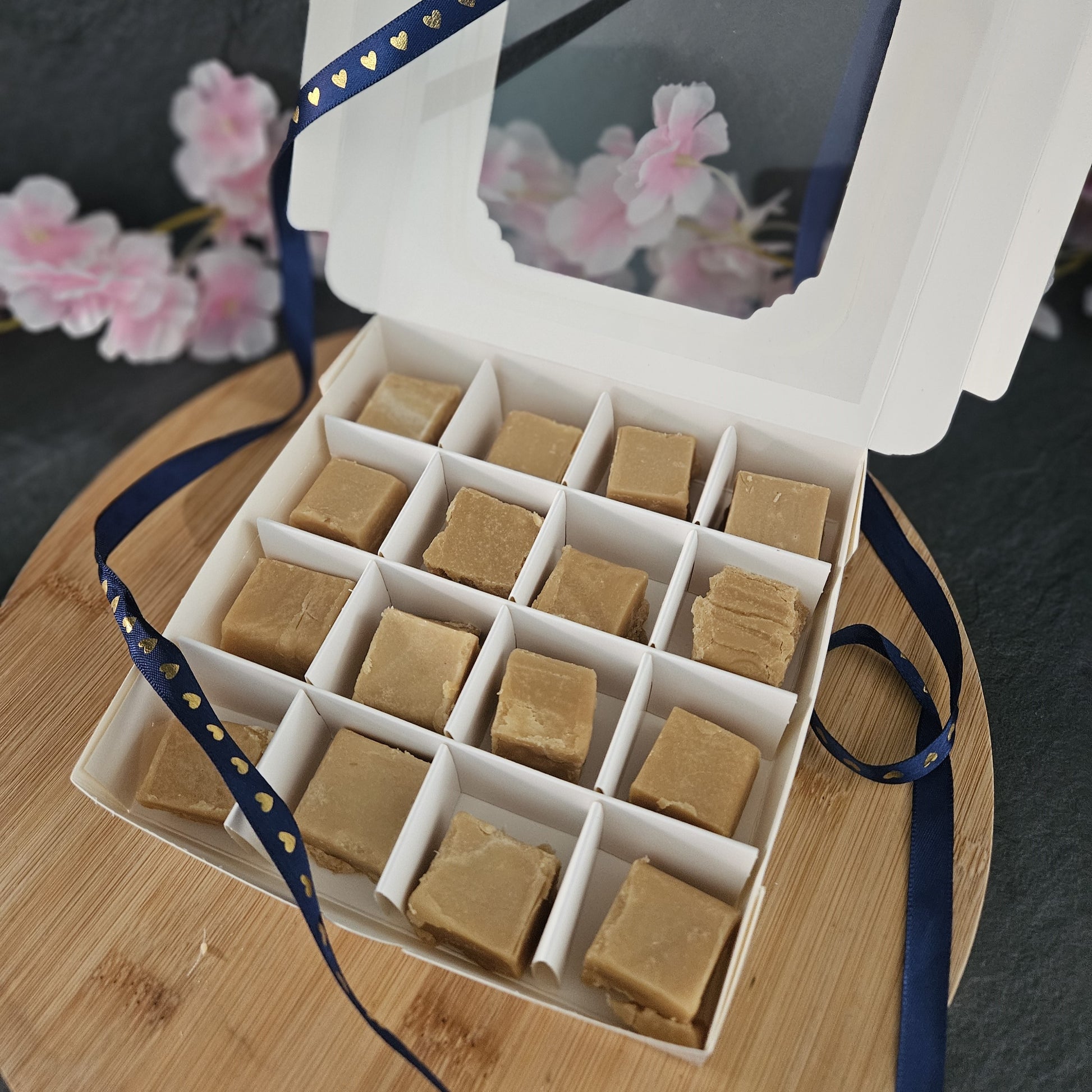 Box of fudge containing 16 pieces with a blue ribbon with gold hearts on a wooden board