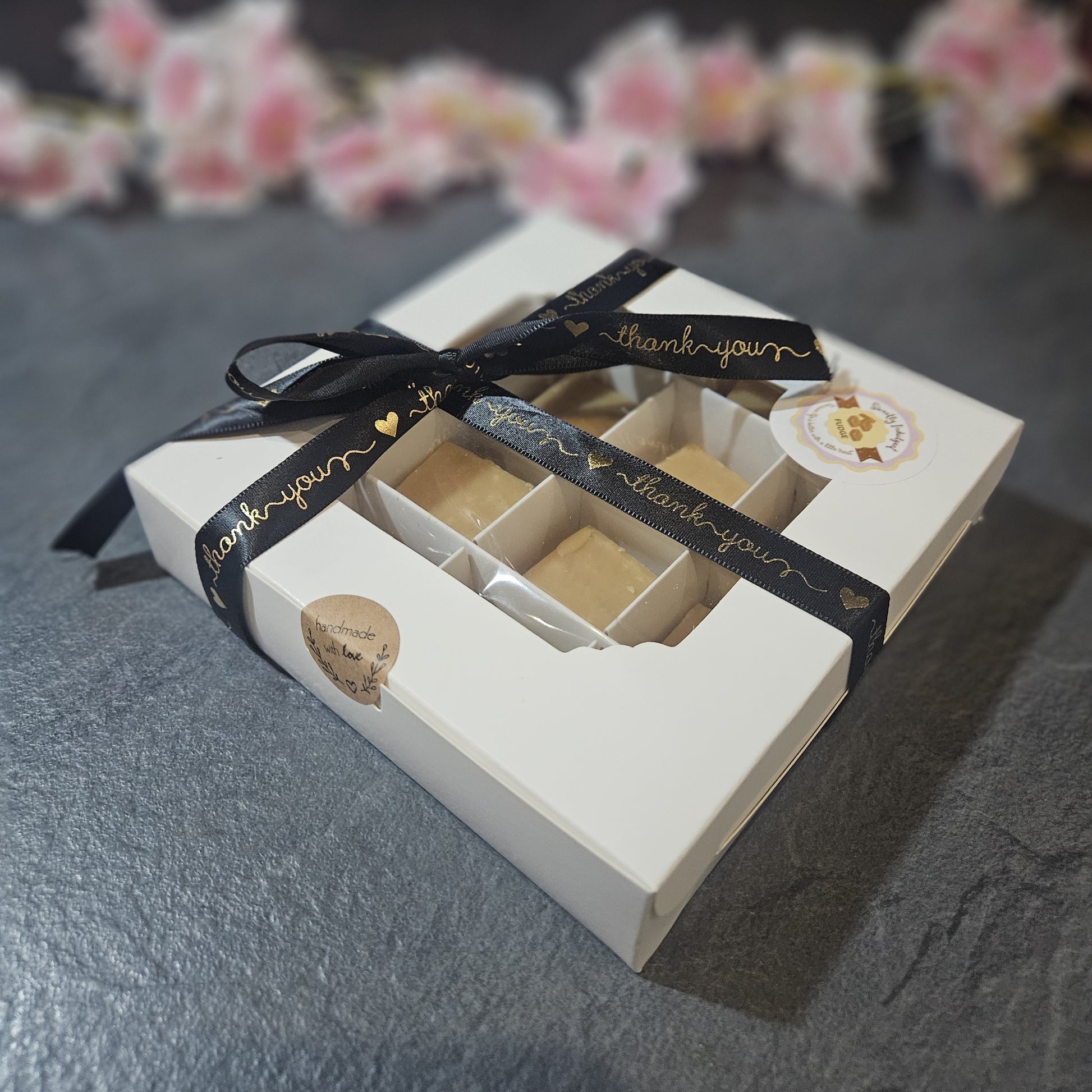 Gift box with fudge and 'thank you' ribbon on a dark surface. sealed with handmade with love sticker and sweetly indulgent branding.