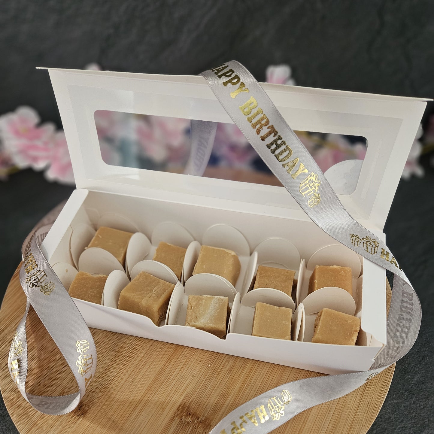 White gift box with grey happy birthday ribbon on a wooden board.