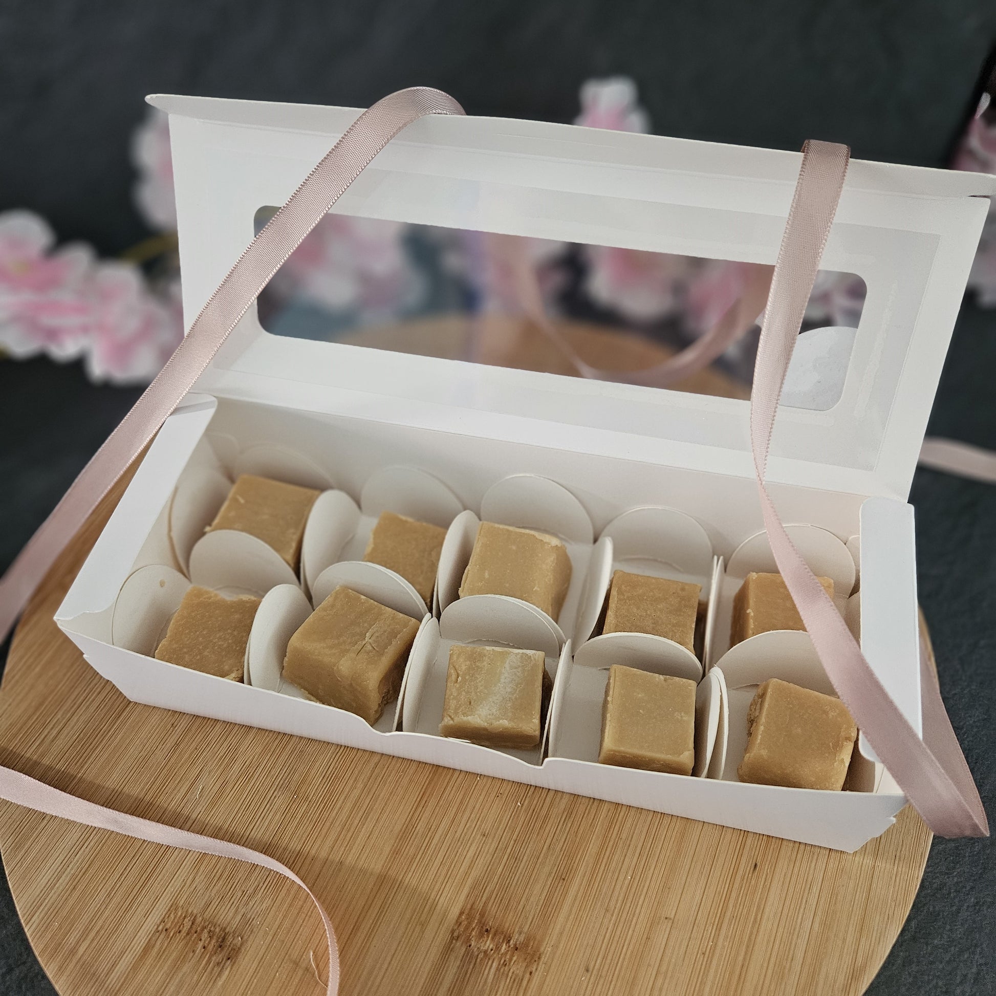 Open white gift box with square fudge on a wooden surface and pink ribbon