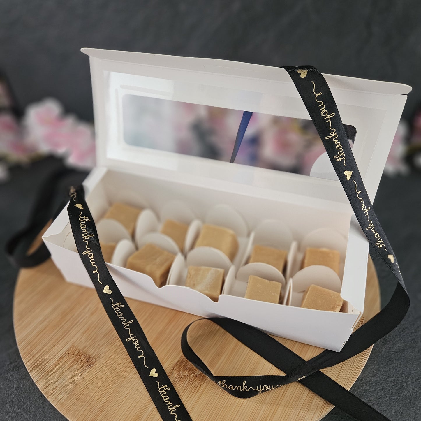 Box of fudge pieces with a black ribbon and gold writing on a wooden board
