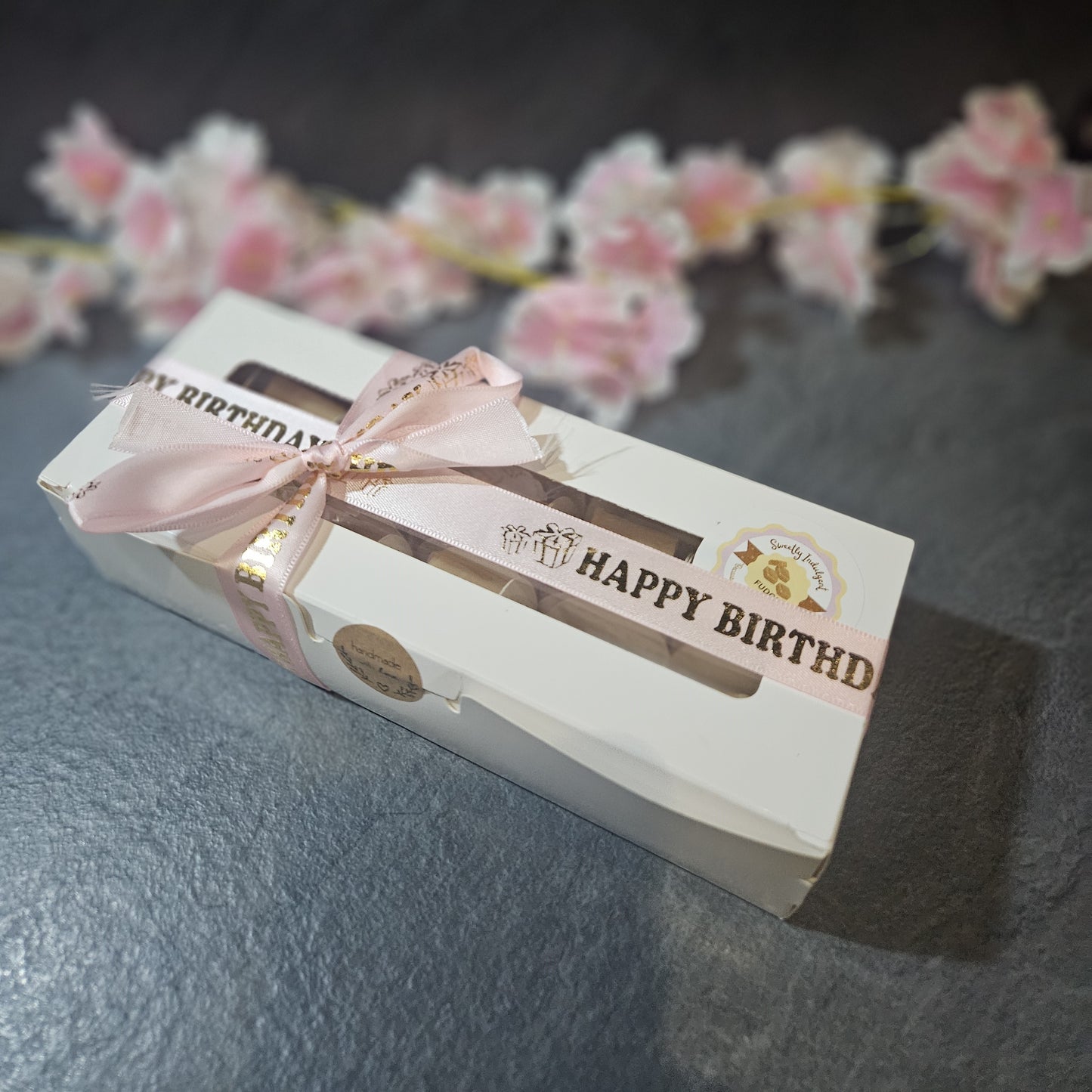 Gift box with 'Happy Birthday' text and pink ribbon on a grey surface.