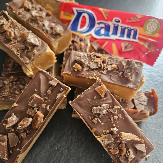Buttery fudge bar topped with milk chocolate and Dime pieces with a red Daim packaging in the background