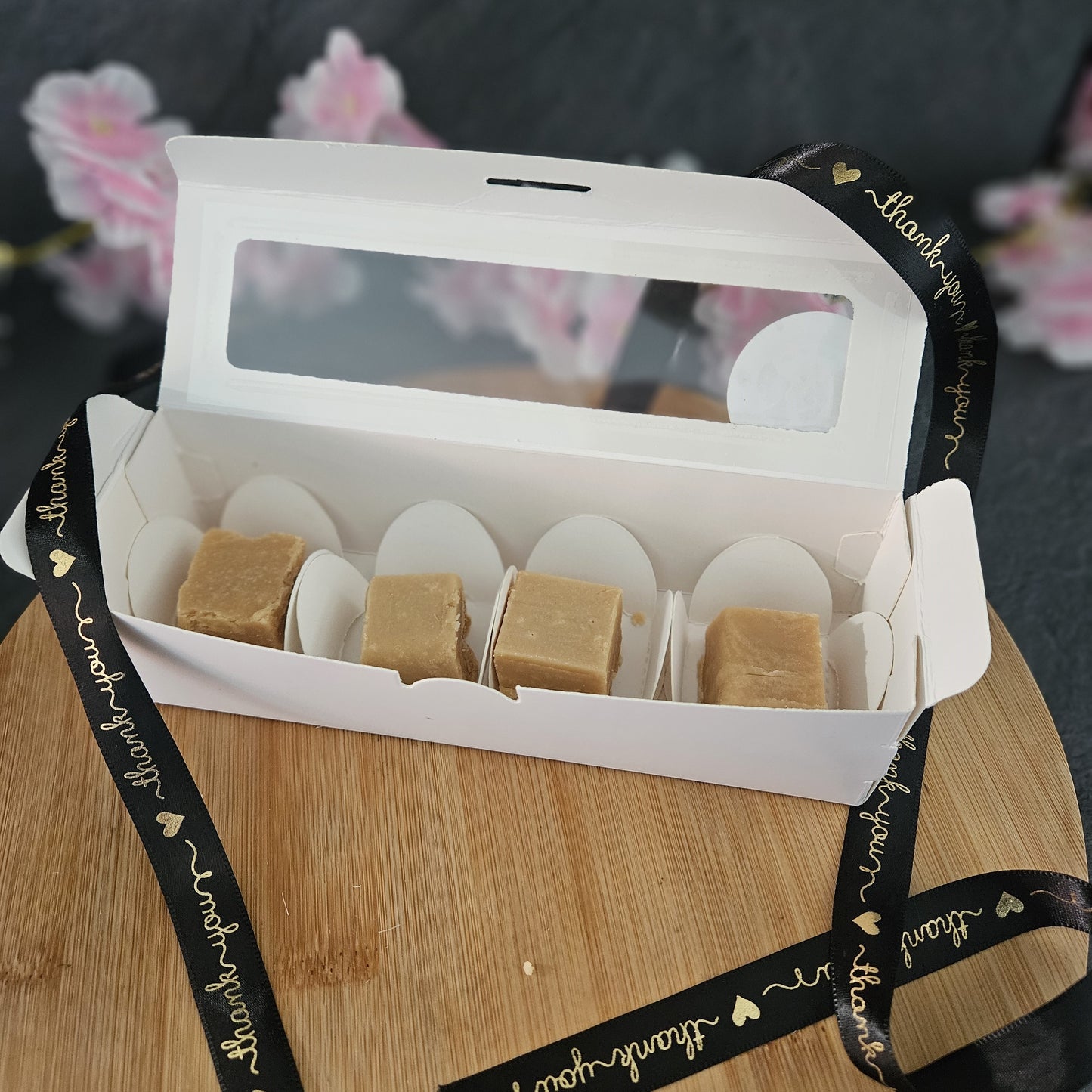 Open box of fudge with a black ribbon with gold thank you text on a wooden surface
