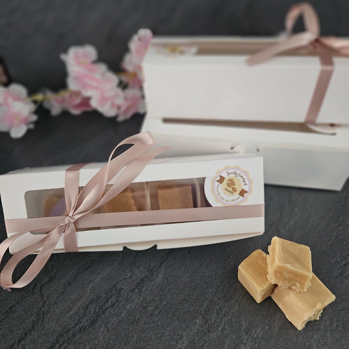Gift box with fudge and a ribbon on a dark surface with sweetly indulgent sticker.