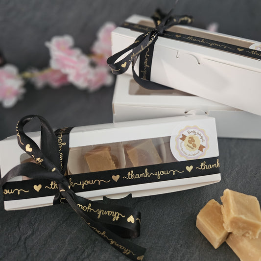 Small box of fudge with a black ribbon and 'thank you' text on a dark surface. Fudge pieces in foreground. 